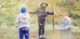 Syntolkning: Två barn och en vuxen leker bland höstlov i skogen